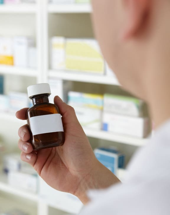 a man holding a bottle of prescription medication in a pharmacy aisle