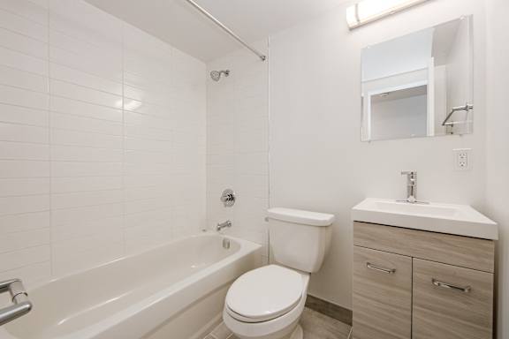 A white bathroom with a toilet, sat 111 Cosburn, Ontario, M4J 2L1 ink, and bathtub.