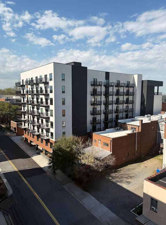 A modern apartment building with balconies is situated on a street corner.