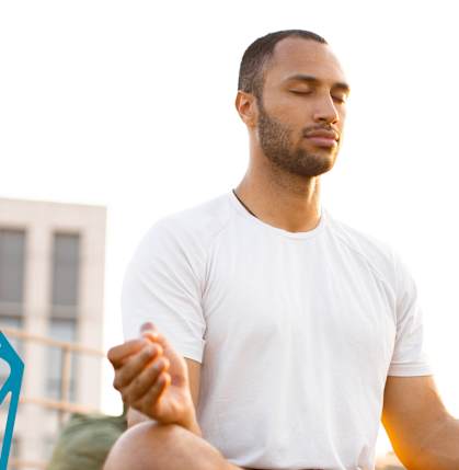 A man in a white shirt is meditating outdoors.