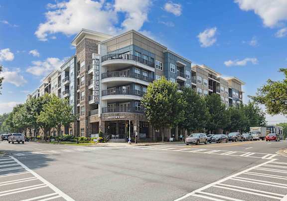 A street view of a multi-story apartment building with cars parked in front.