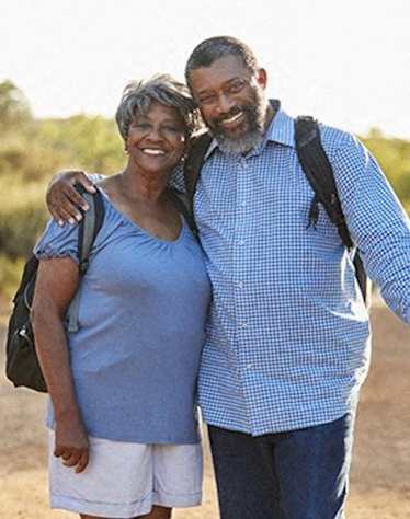 An older couple are standing outside and smiling.