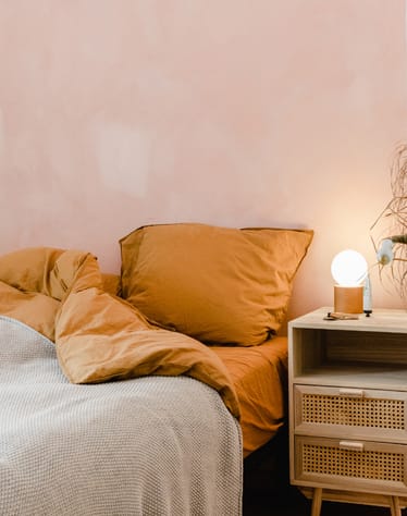 a bedroom with an unmade bed with orange pillows and a nightstand with