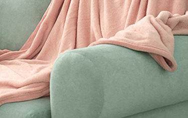 A pink blanket is draped over a green couch.