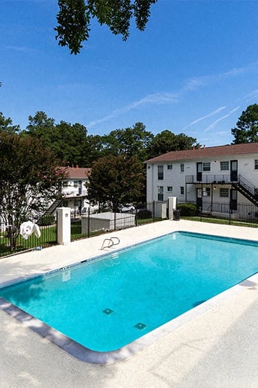 our resort style swimming pool is surrounded by blue chairs and trees