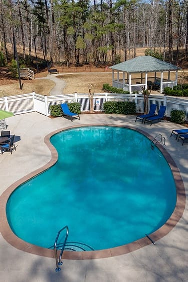 our resort style swimming pool is surrounded by blue chairs and trees