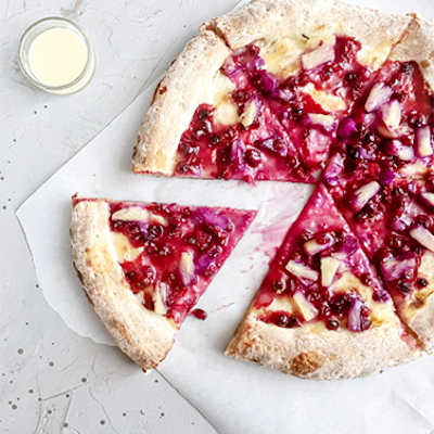 A pizza with a white crust topped with red fruit and nuts.