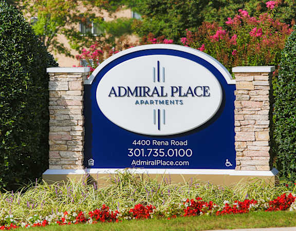 A sign for Admiral Place Apartments is displayed in front of some flowers.
