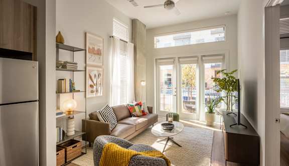 A modern living room with a grey sofa, a yellow throw blanket, and a ceiling fan.