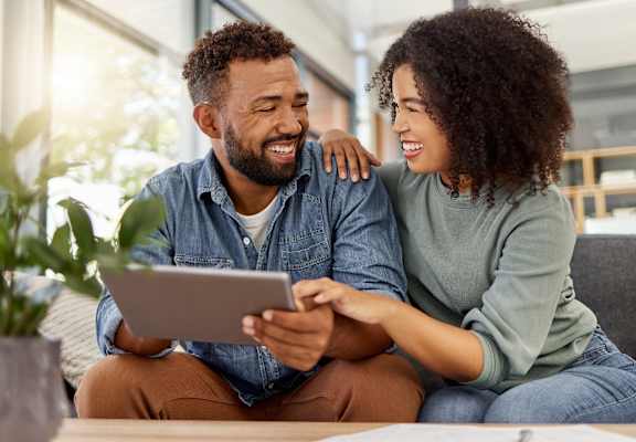 a man and woman sitting on a couch looking at a tablet computer
