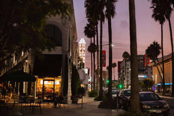 a city street at night with palm trees and cars parked on the side of the road