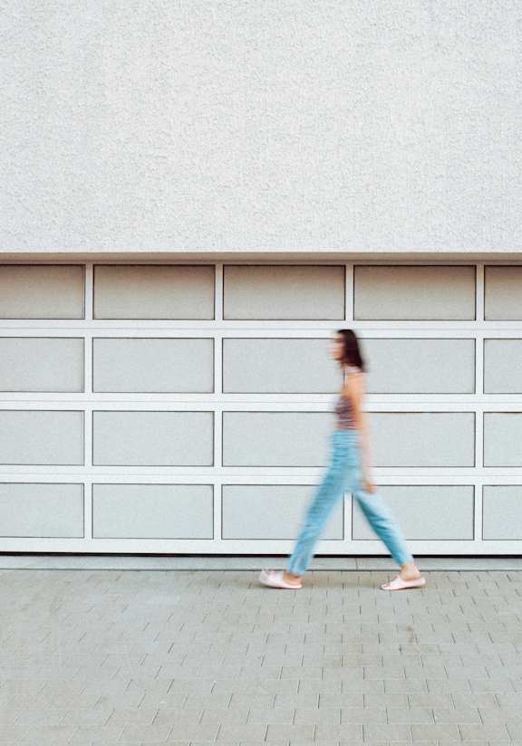 A woman in blue jeans and pink shoes is walking in front of a white garage door.
