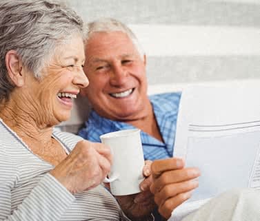 an older couple sitting on a couch drinking coffee and looking at a magazine