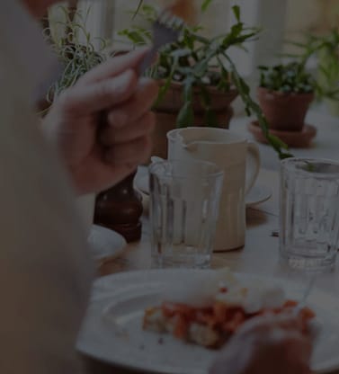 A person is eating a meal at a table with a cup and a plate of food.