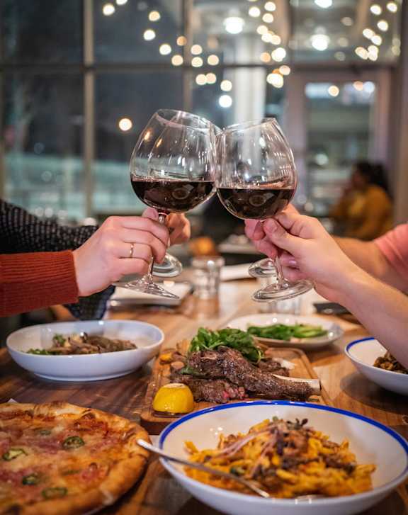 Two people toasting with wine glasses in front of a table full of food.