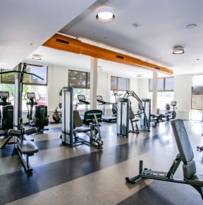 a gym with cardio machines and other exercise equipment in a building with windows