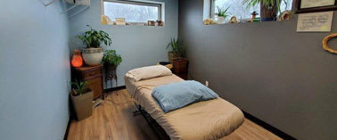 A small bedroom with a bed, a window, and a shelf with plants.