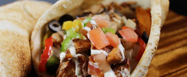 A pita sandwich with chicken, tomatoes, and olives.