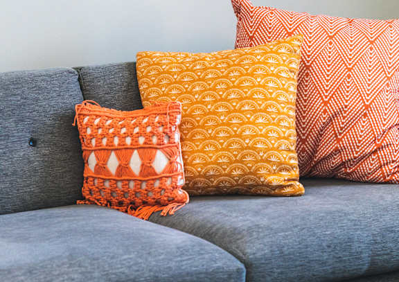A grey couch with three pillows and a chess board on a table.