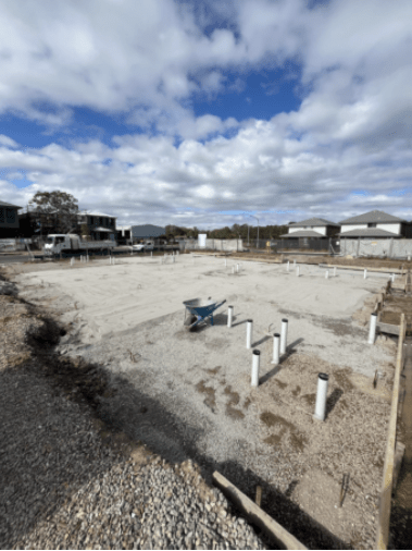 A construction site with a blue wheelbarrow and white poles in the foreground.