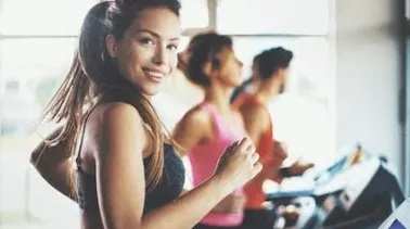 A woman in a pink tank top is running on a treadmill in a gym.