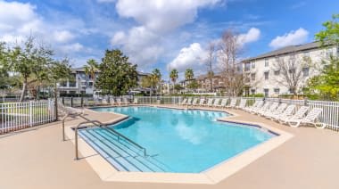 A large outdoor swimming pool surrounded by a metal fence and lounge chairs. at The Villages on Millenia Apartments, Orlando, FL, 32839