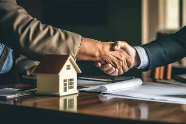 a handshake over a table with a model house on it