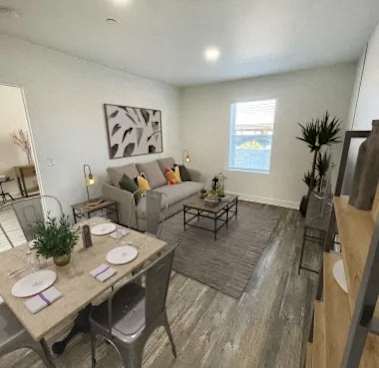 A dining area with a table set for two and a couch with pillows in the background.
