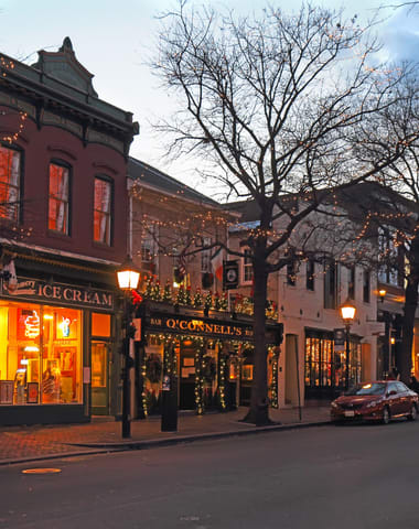 a city street at dusk with christmas lights on the buildings