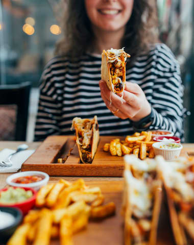 a woman holding a sandwich with fries and dip in front of her