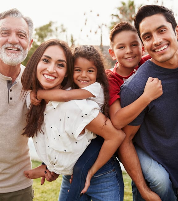 A family of five is standing together outside with a tree in the background.