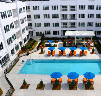 a resort style pool with blue umbrellas in front of an apartment building