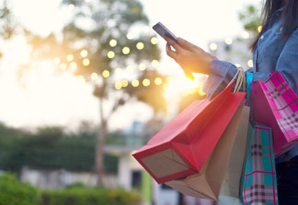 a woman holding shopping bags and looking at her cell phone