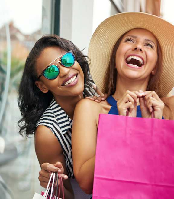 Two women are laughing and holding shopping bags.