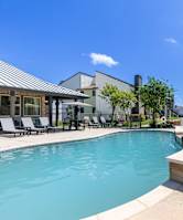 A swimming pool surrounded by a patio with chairs and a building in the background.