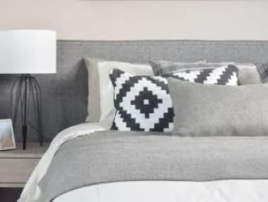 A bed with a grey headboard and a white comforter with four decorative pillows.