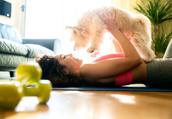 Young girl in sportswear playing with her dog at home on floor while attempting to work out 