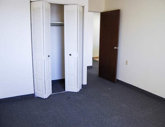 A room with a carpeted floor and a white door with a shelf.