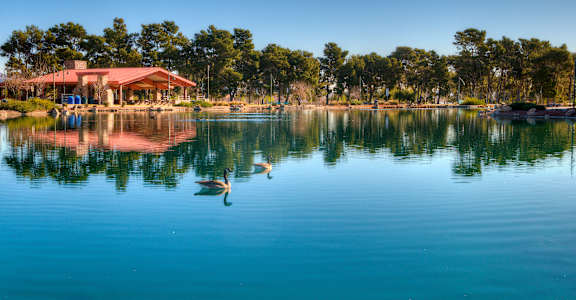 A serene lake with a building and trees in the background.