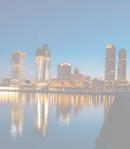 A city skyline at dusk with buildings reflected in the water.