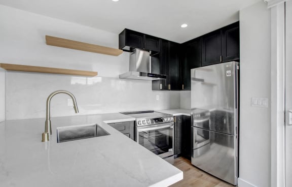 a kitchen with white countertops and black cabinets and a stainless steel refrigerator