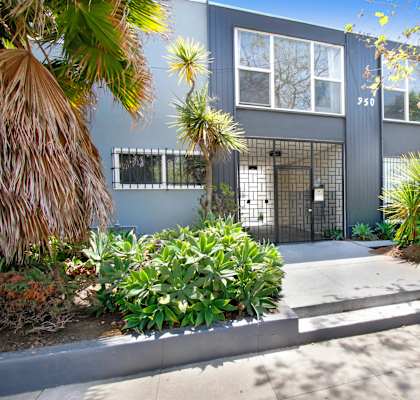 the front of a blue house with a sidewalk and plants in front of it