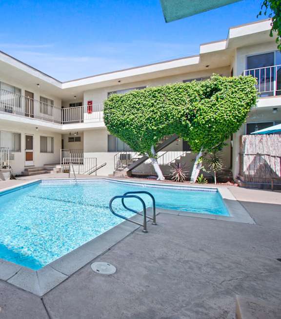 A pool surrounded by a white building and a green tree at Oasis Apartments, Burbank, California