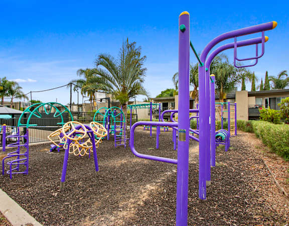 A playground with purple and yellow equipment and palm trees in the background