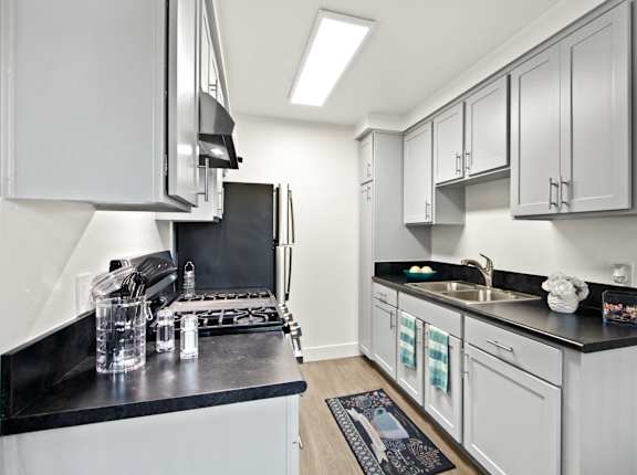 A kitchen with white cabinets and black countertops  at Clair Del and Clair Del Gardens, Long Beach, California