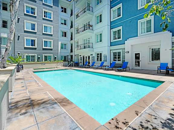 a swimming pool with blue chaise lounge chairs and an apartment building in the background at Apex Mission Valley, San Diego, 92108