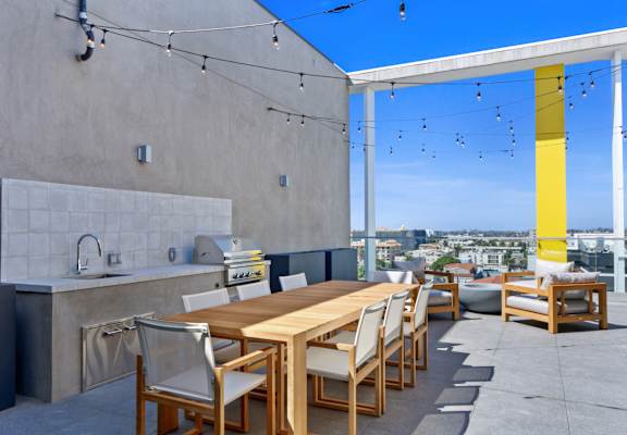 a long wooden dining table with white chairs sits on a concrete patio with a kitchen counter and