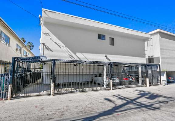 a white building with a gate and parked cars in front of it