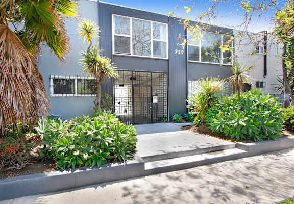 the front of a blue house with a sidewalk and plants in front of it