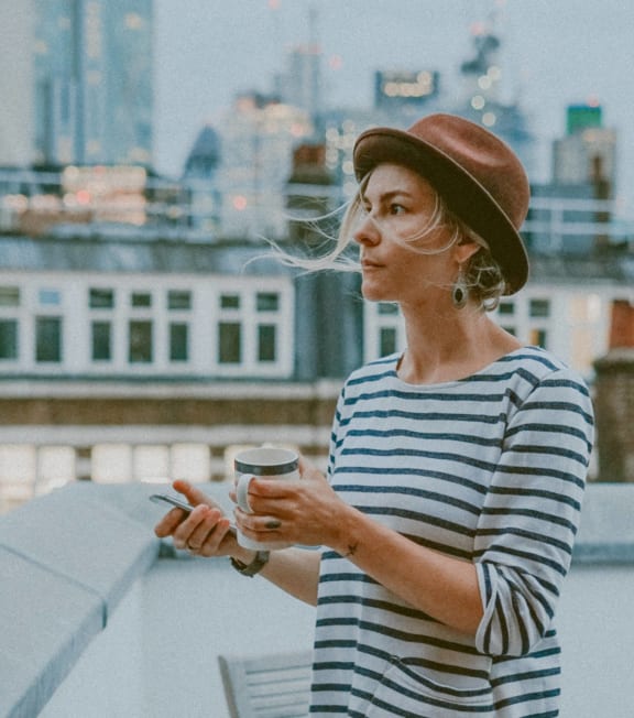 a woman standing on a roof holding a coffee cup and a cell phone
